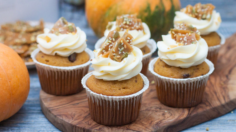 Five cupcakes with buttercream frosting on wooden tray