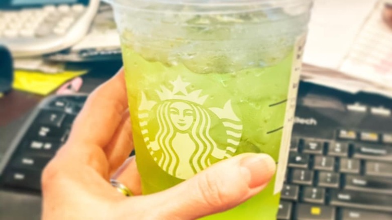 Person holding a green iced drink from Starbucks