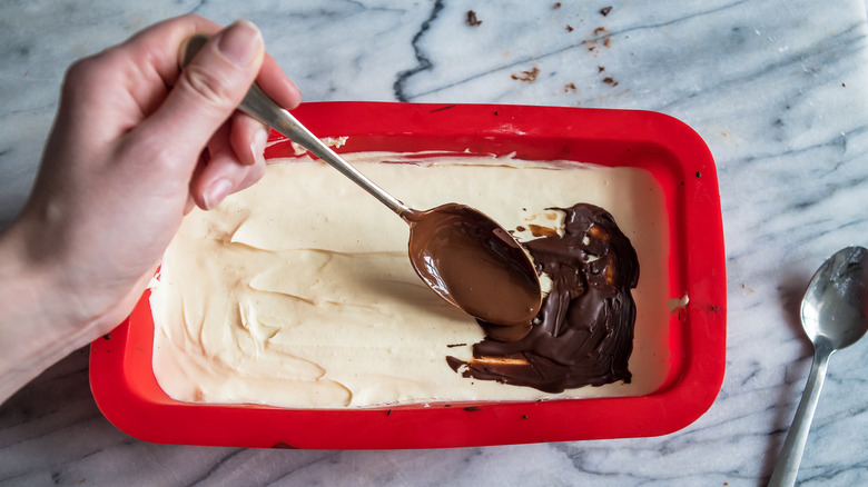 melted chocolate drizzled across whipped cream filling in a red silicone loaf pan