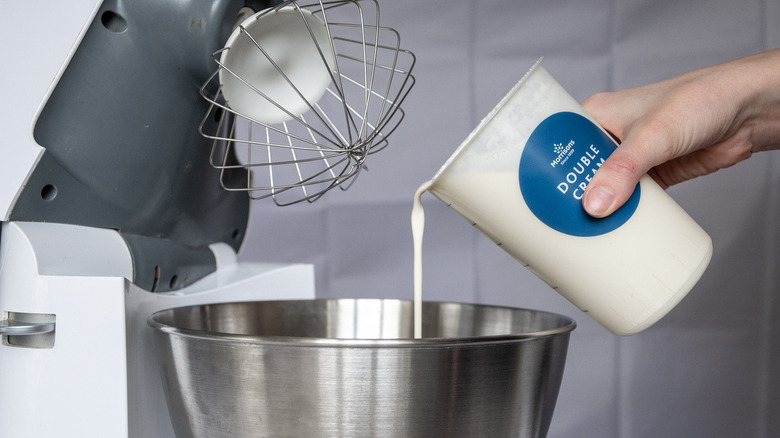 whipped cream being poured into a stand mixer's bowl