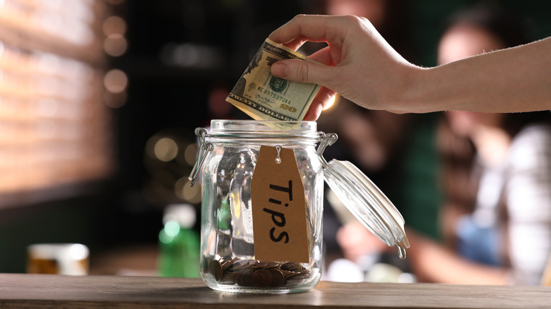 hand adding money to tip jar