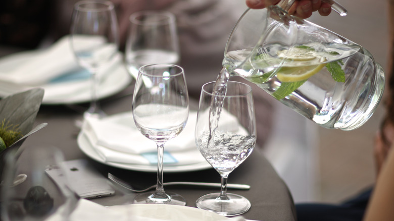 Person pouring water into glass at restaurant table