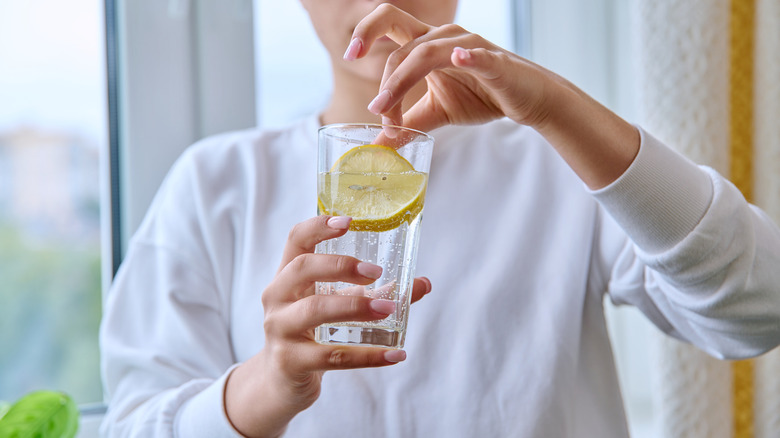 Woman adding lemon to glass of water