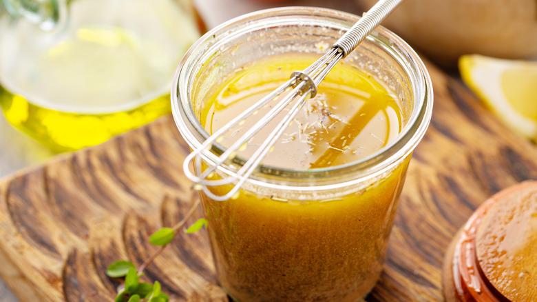 A jar of marinade with a whisk on a wood cutting board