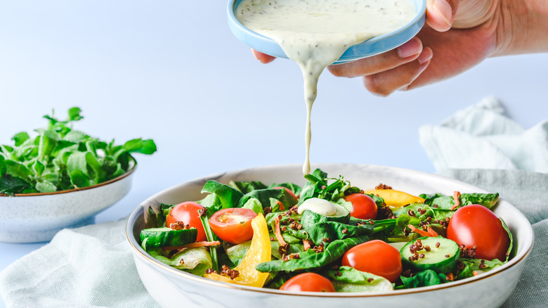 A bowl of salad greens being topped with salad dressing