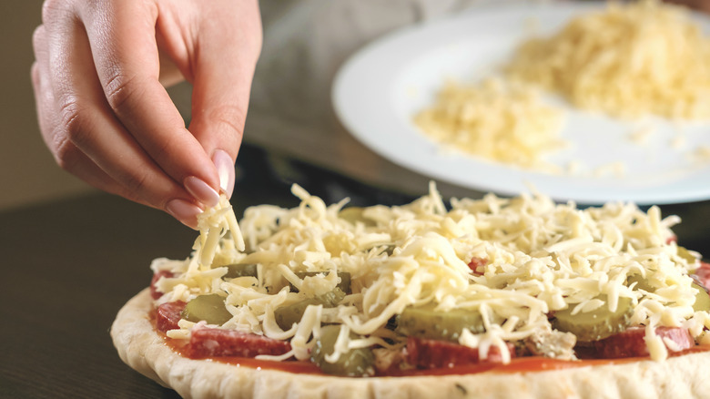 hand adding cheese to raw pizza