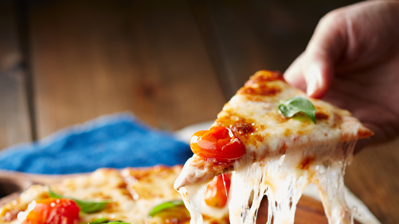 hand pulling up slice of hot pizza