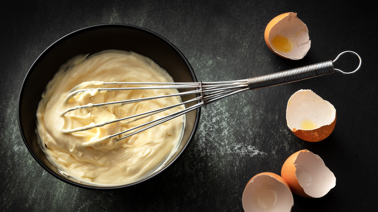 mayonnaise in a bowl with hand whisk and egg shells on the side