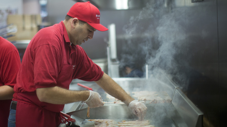 Employee cooking bacon at Five Guys