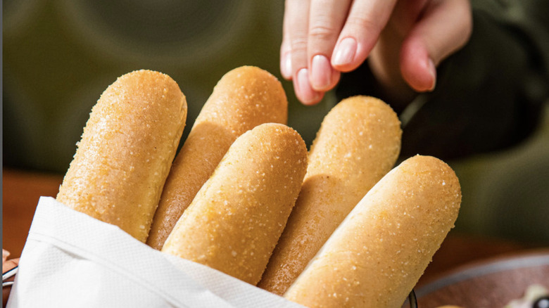 A hand reaches for Olive Garden breadsticks