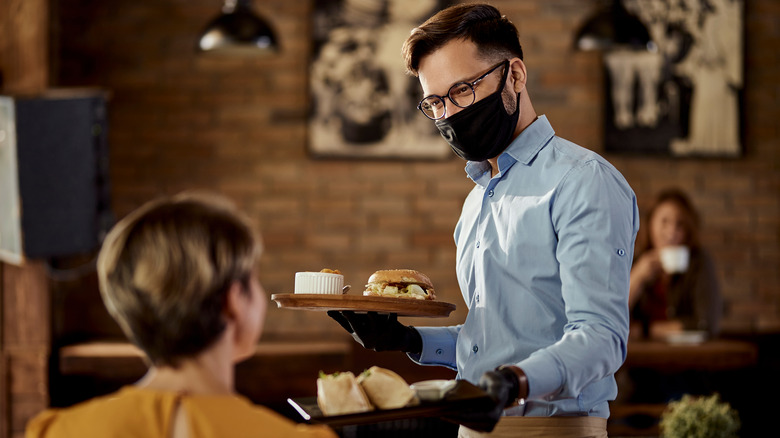 Waiter with mask on carrying plates of food