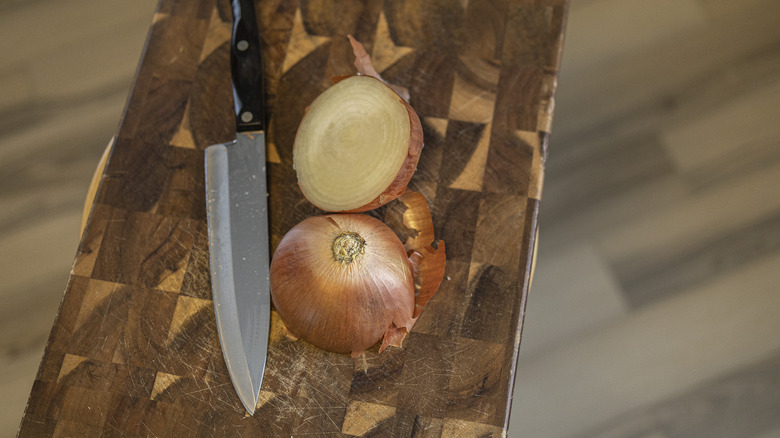 Onion cut in half and knife on wooden cutting board