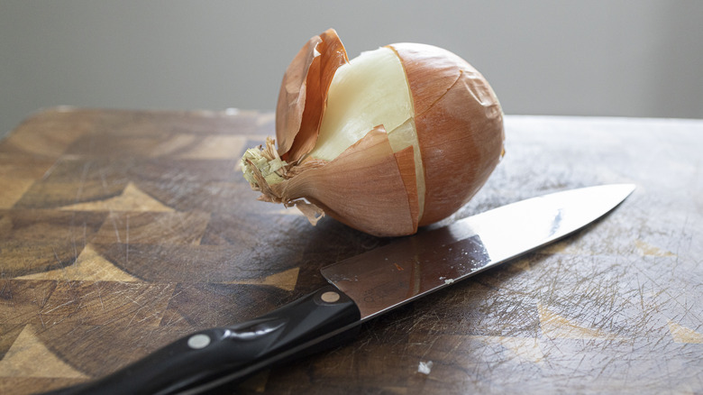 Half unwrapped onion on cutting board with knife