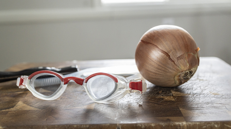 Onion and swimming goggles next to knife on cutting board