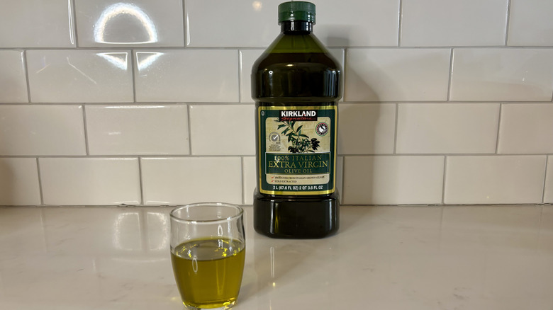 a green bottle of extra virgin olive oil with glass of olive oil