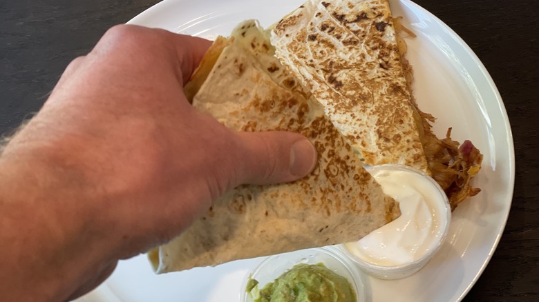 a hand dipping a quesadilla in sour cream