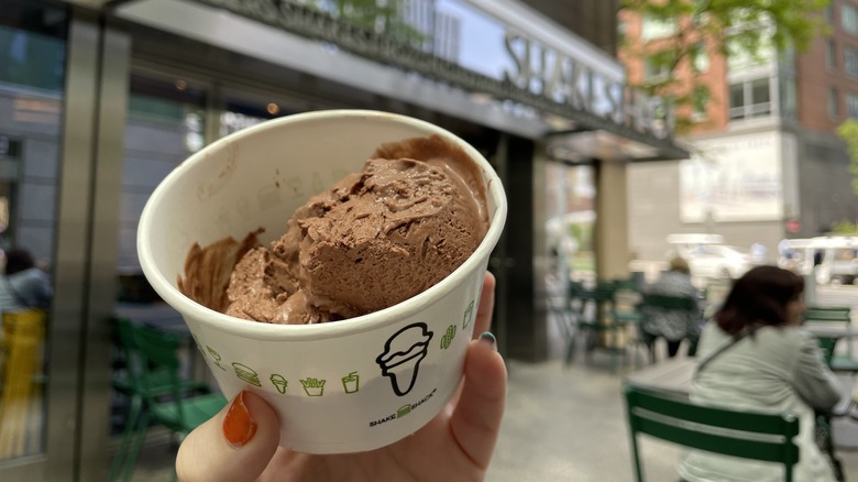 a hand holding a cup of plant-based chocolate frozen custard from shake shack