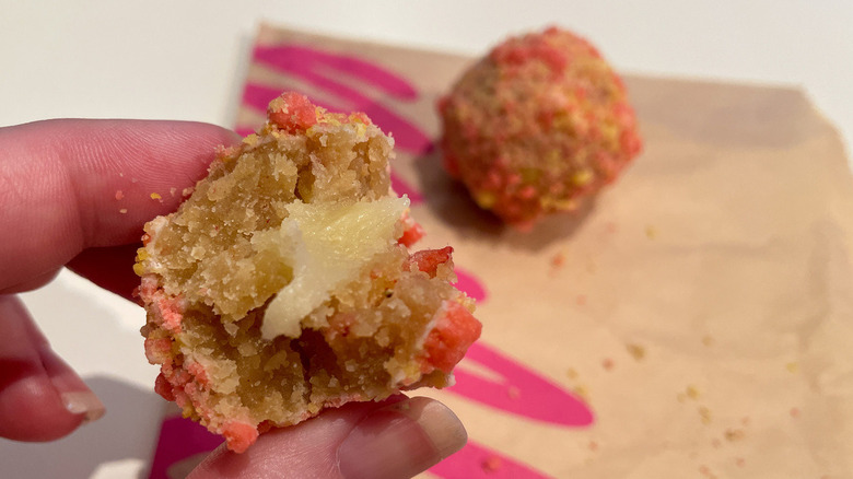 A Milk Bar Taco Bell Strawberry Bell Cake Truffle with a bite taken out of it.