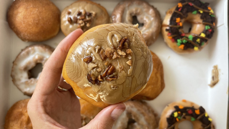 holding krispy kreme Maple Pecan Cheesecake donut