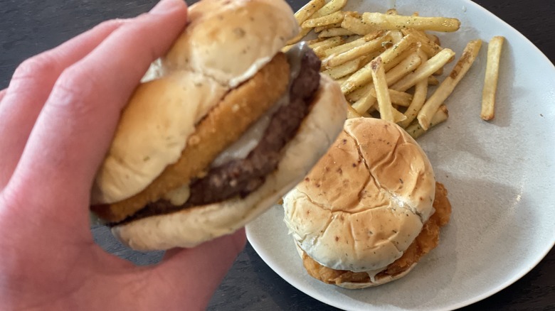 a hand holding a burger above a sandwich and fries