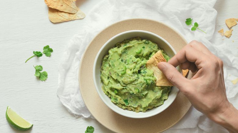 hand dipping chip in guacamole