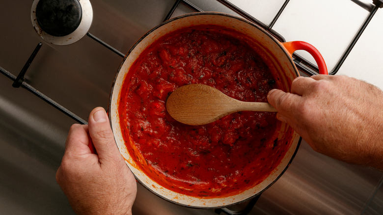 hand stirring tomatoes in pot