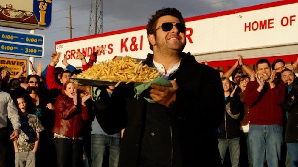 Adam Richman holding platter of fries in front of cheering crowd