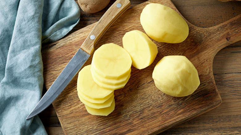 A peeled and cut potato on cutting board with knife