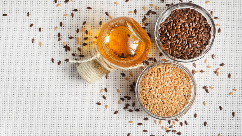 Flaxseeds on white background next to bottle of oil