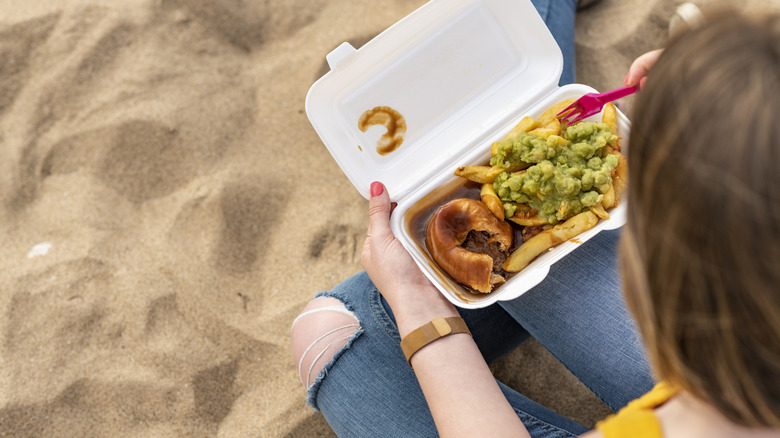 A person eating chips and mushy peas on the beach