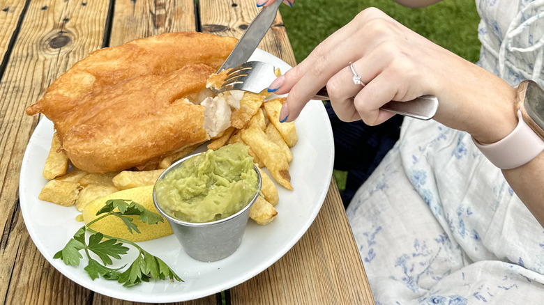 A person eating a plate of food containing a side dish of mushy peas