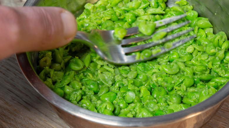 A fork mashing green peas