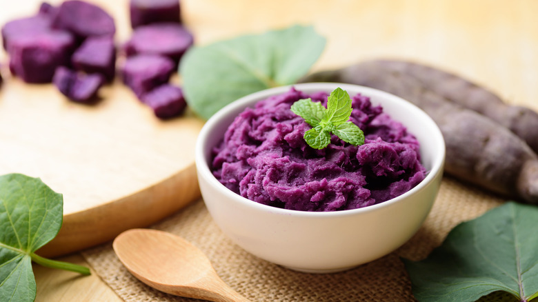 bowl of mashed purple potatoes with mint leaf garnish in white bowl