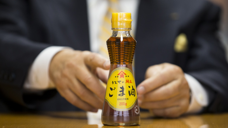A bottle of sesame oil with person's hands in background
