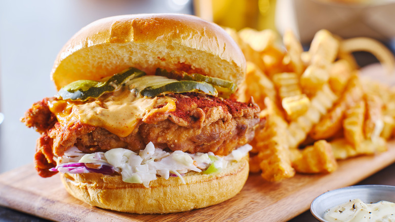 Spicy chicken sandwich overflowing with sauce and coleslaw with a side of crinkle cut fries