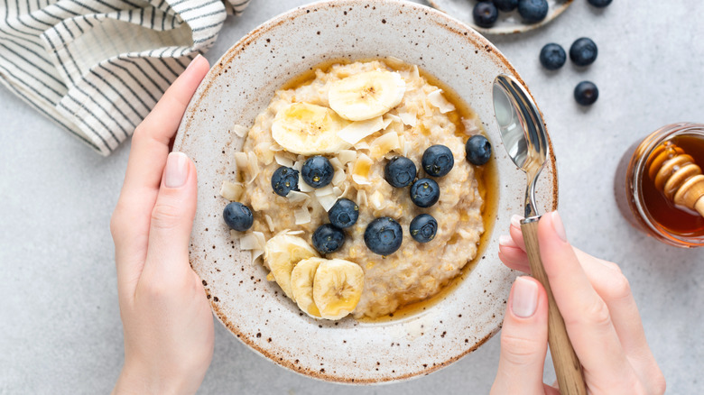 Hands holding bowl of oatmeal with fruits and spoon
