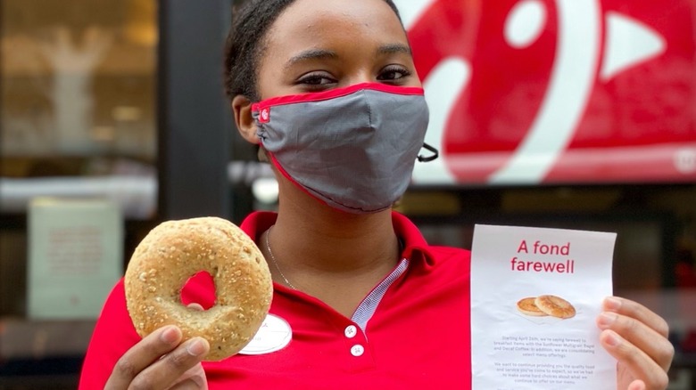 Chick-fil-A employee in mask holding bagel and sign