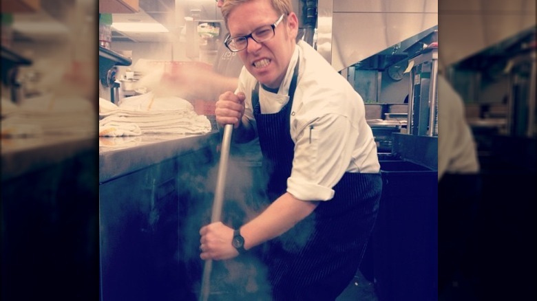 Chef Jason Stude grinning with a broom in his hands