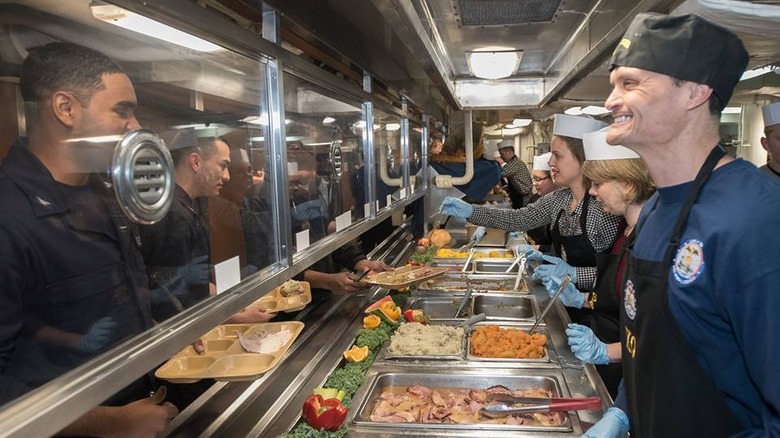 US Navy chefs smiling at sailors entering the food line