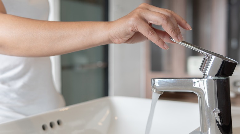 hand turning on faucet at sink