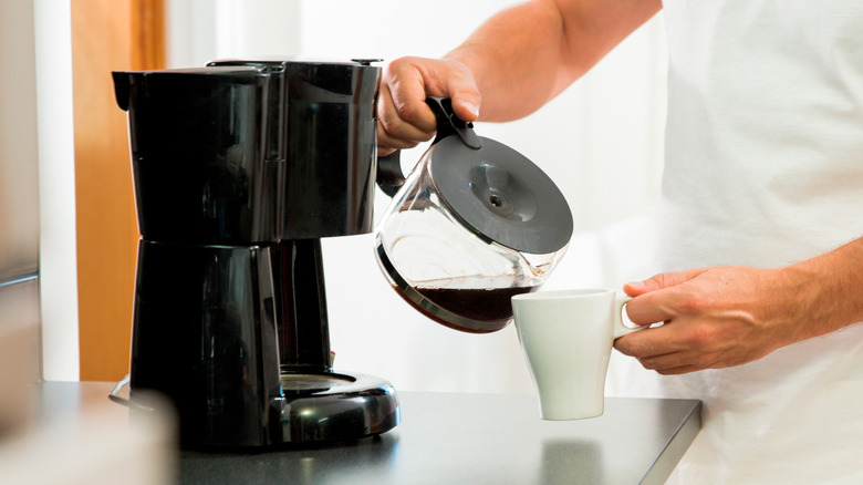 Person pouring coffee into cup, next to coffee maker