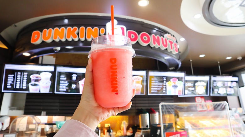 holding a dunkin' donuts drink up to the store's sign