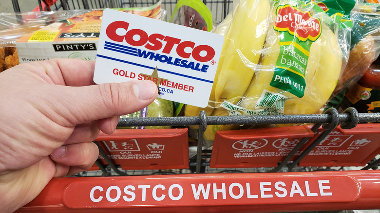 person holding Costco card near cart of groceries