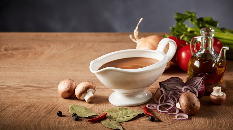 White gravy boat with brown gravy and vegetables in background