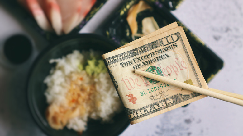 dollar bill between chopsticks with Asian food below