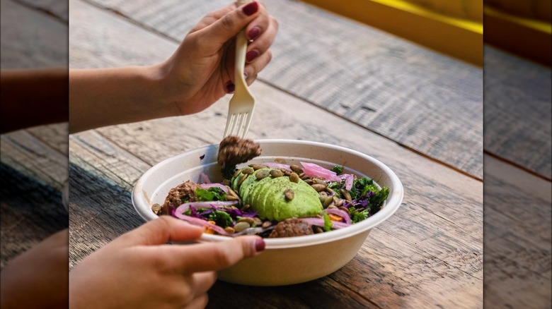 person eating avocado-topped salad in to-go bowl