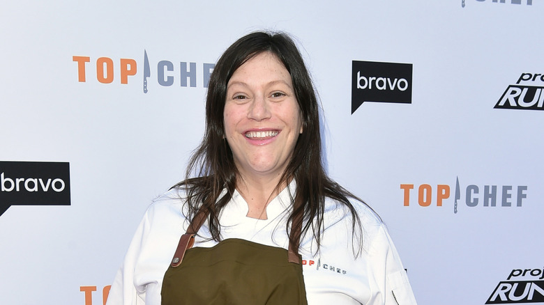 Sara Bradley in chef's whites and an apron standing in front of a Top Chef/Bravo backdrop