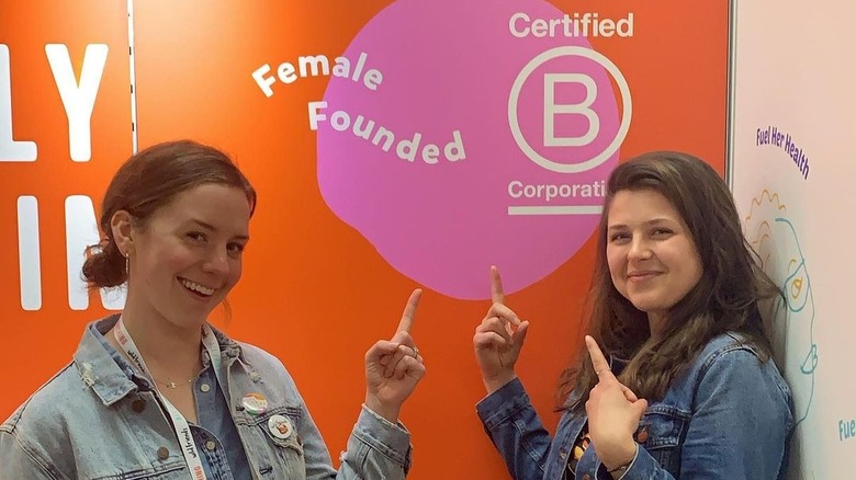 Wild Friends founders posing in front of B Corp sign