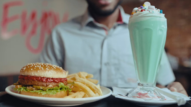 A Wimpy worker holding a burger with a green milkshake.