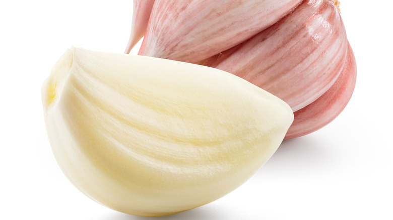 Peeled garlic clove in front of unpeeled garlic clove cluster over white background